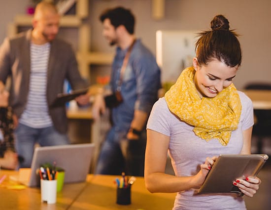 A smiling designer working on a tablet while colleagues talk behind her