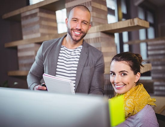Two smiling colleagues making notes together at a computer